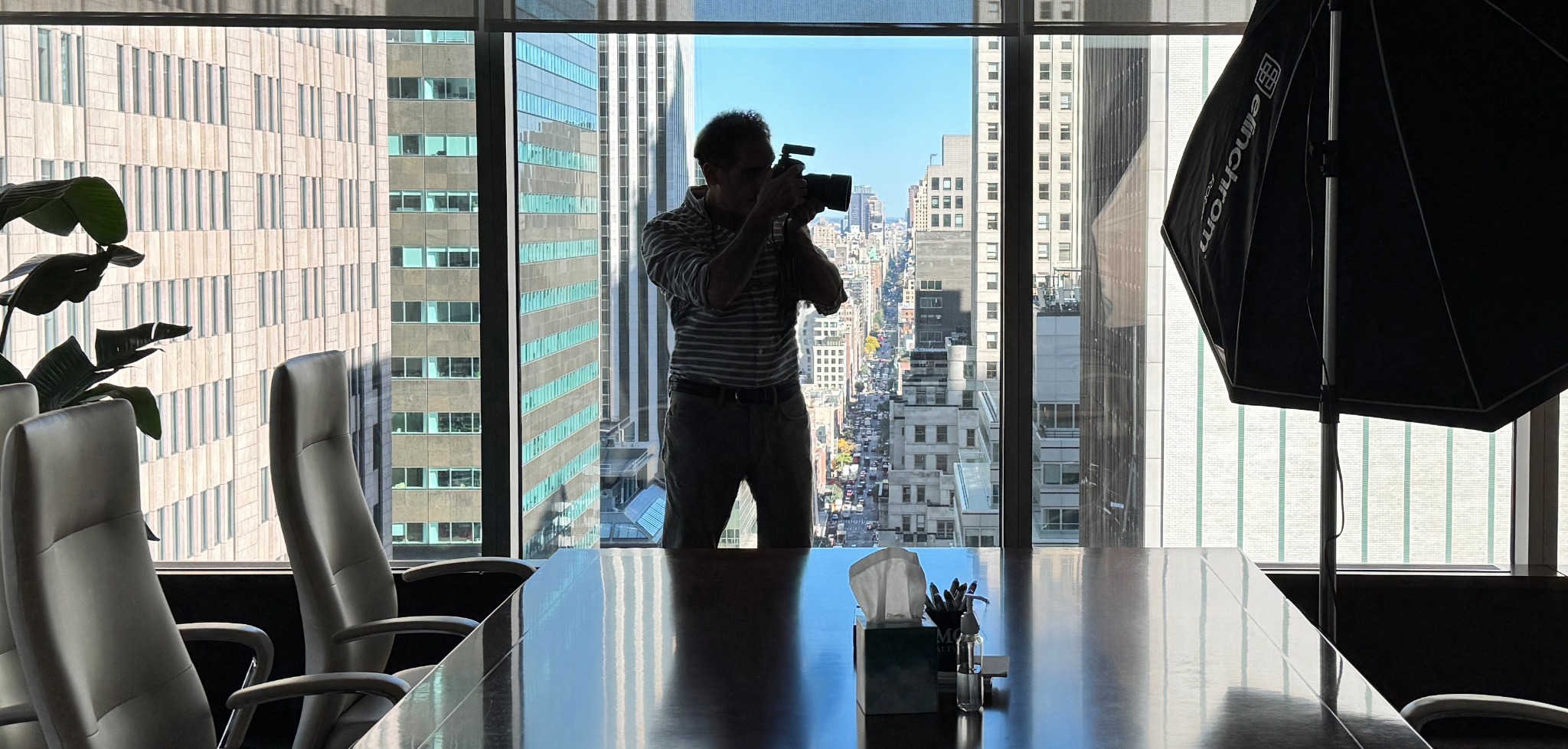 Ron photographing a portrait in a Manhattan office, with the New York skyline beyond the windows
